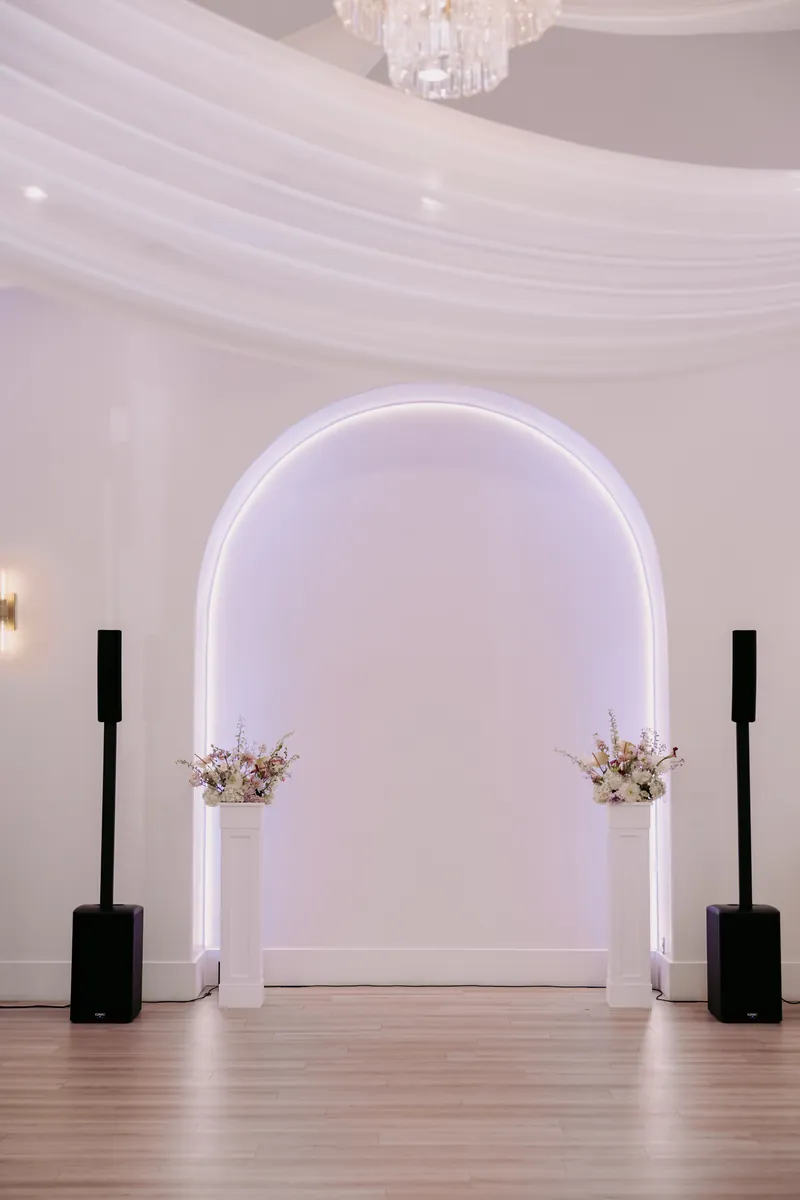Lit ceremony arch with floral pedestals and the onsite sound system at Moments on Main