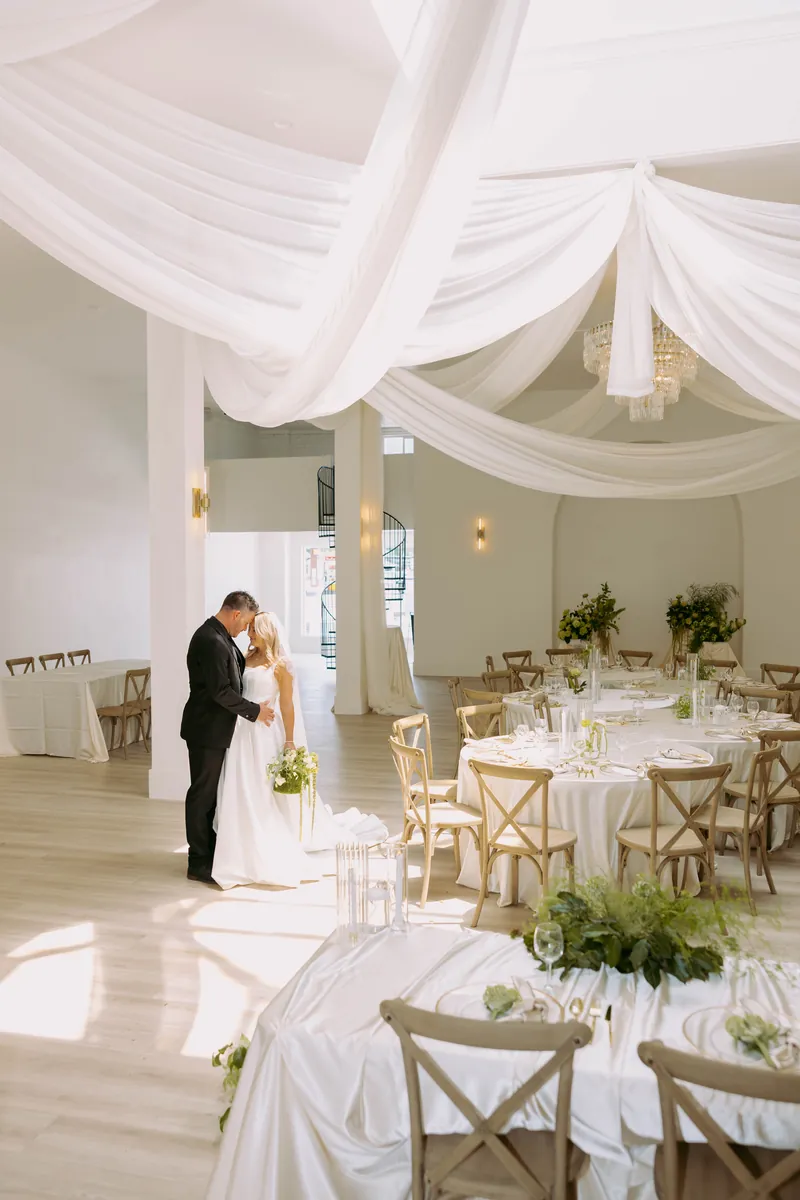 Couple dancing beside set reception tables under ceiling draping at Moments on Main