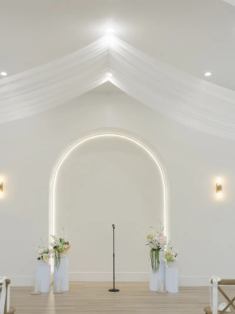 Lit ceremony arch beneath ceiling draping at Moments on Main, Payson
