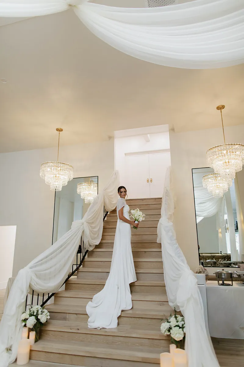 Bride descending the staircase under the chandeliers at Moments on Main