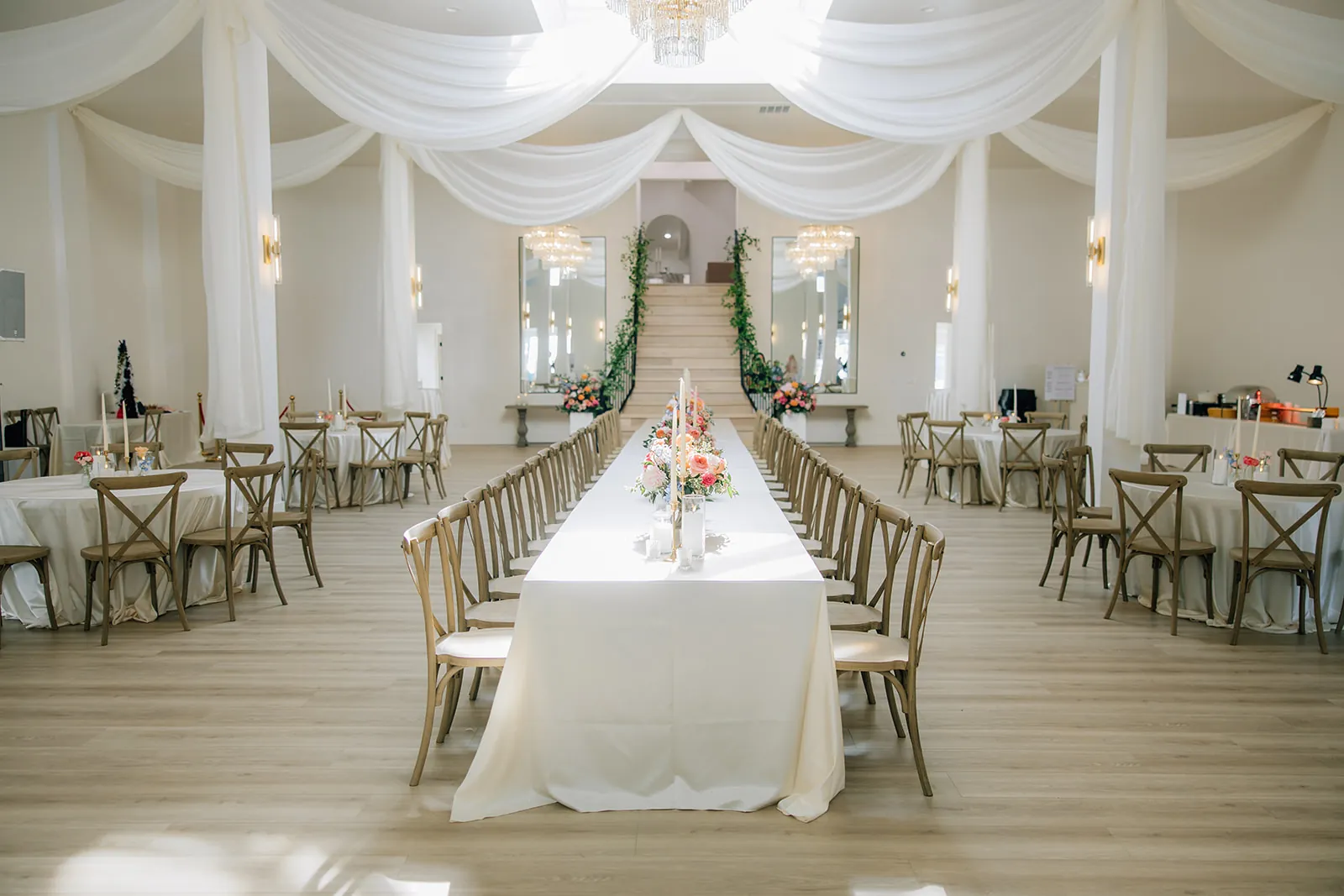 Long banquet table set down the centre of the main room at Moments on Main, ceiling draping and chandeliers above and the staircase beyond