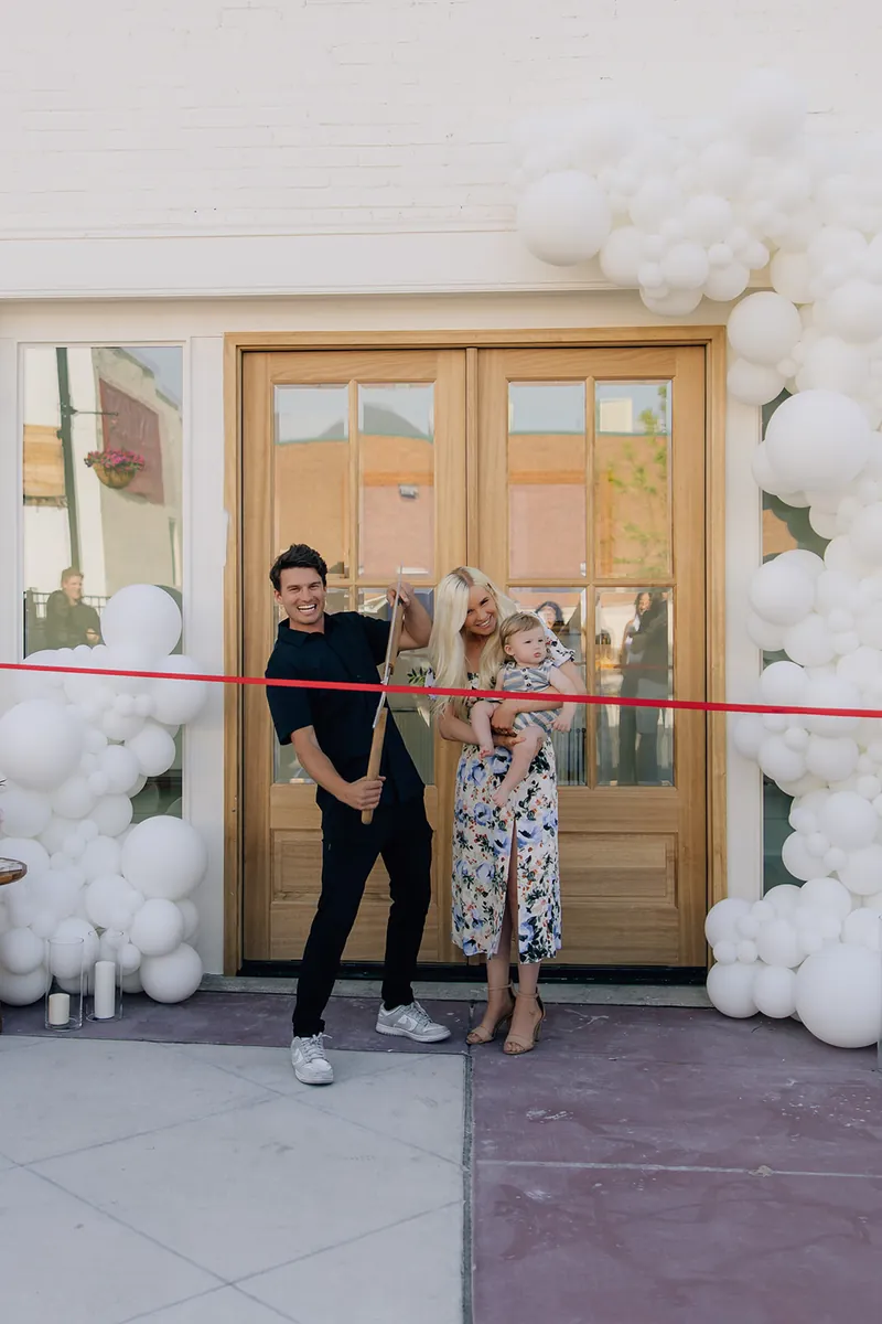 Family at the front doors of Moments on Main beneath a white balloon arch, Payson